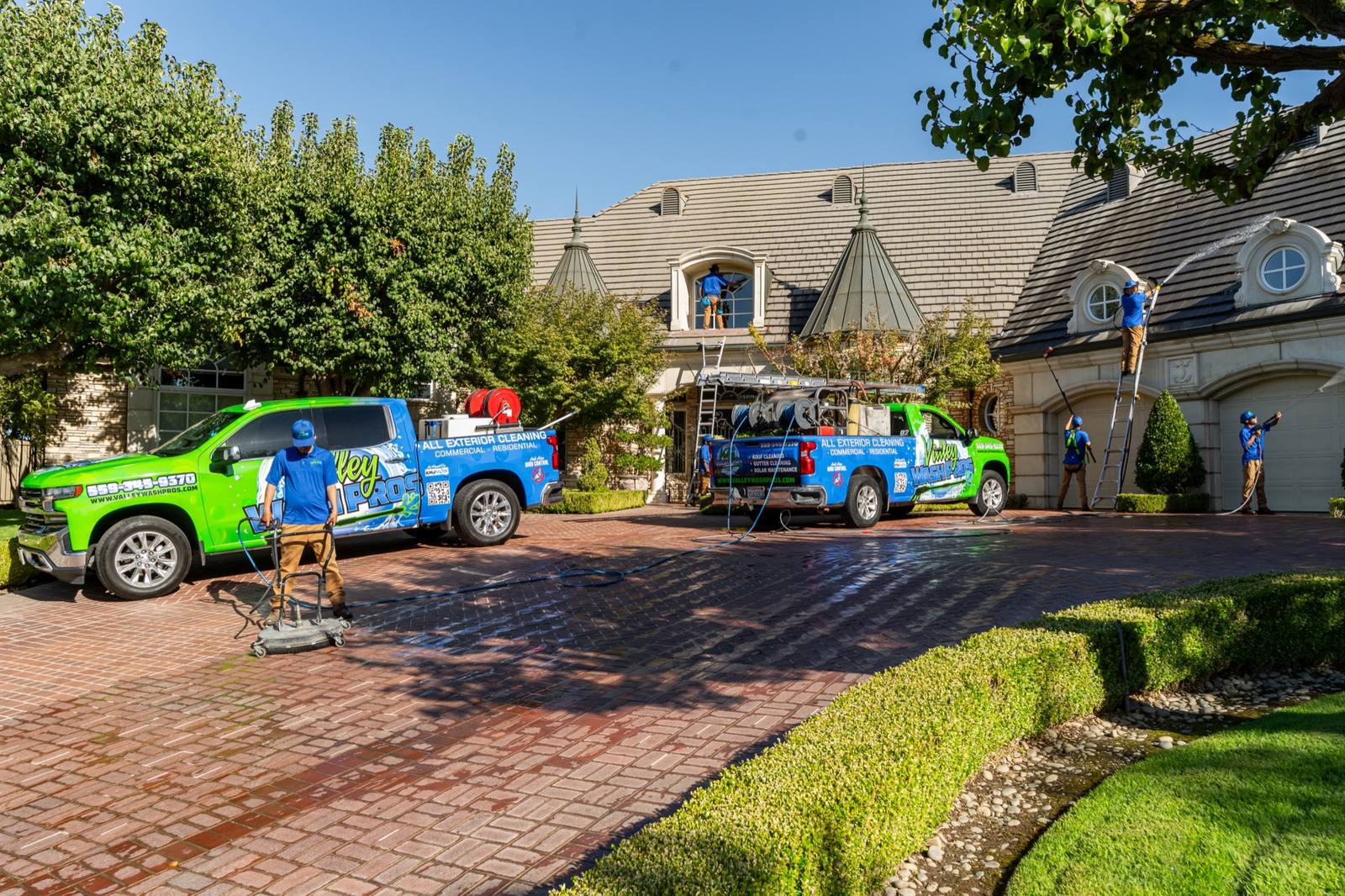 Two wrapped trucks on an estate driveway with technicians cleaning windows and hardscape