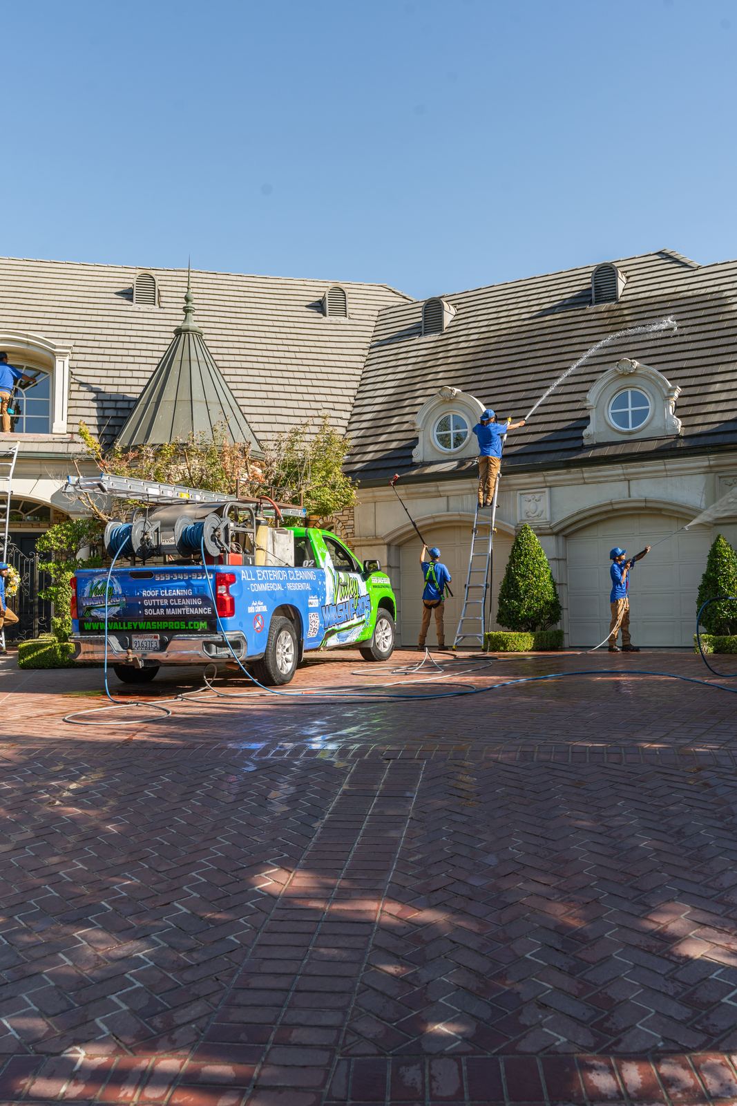 Technician on an extension ladder soft washing the upper story of a large estate home