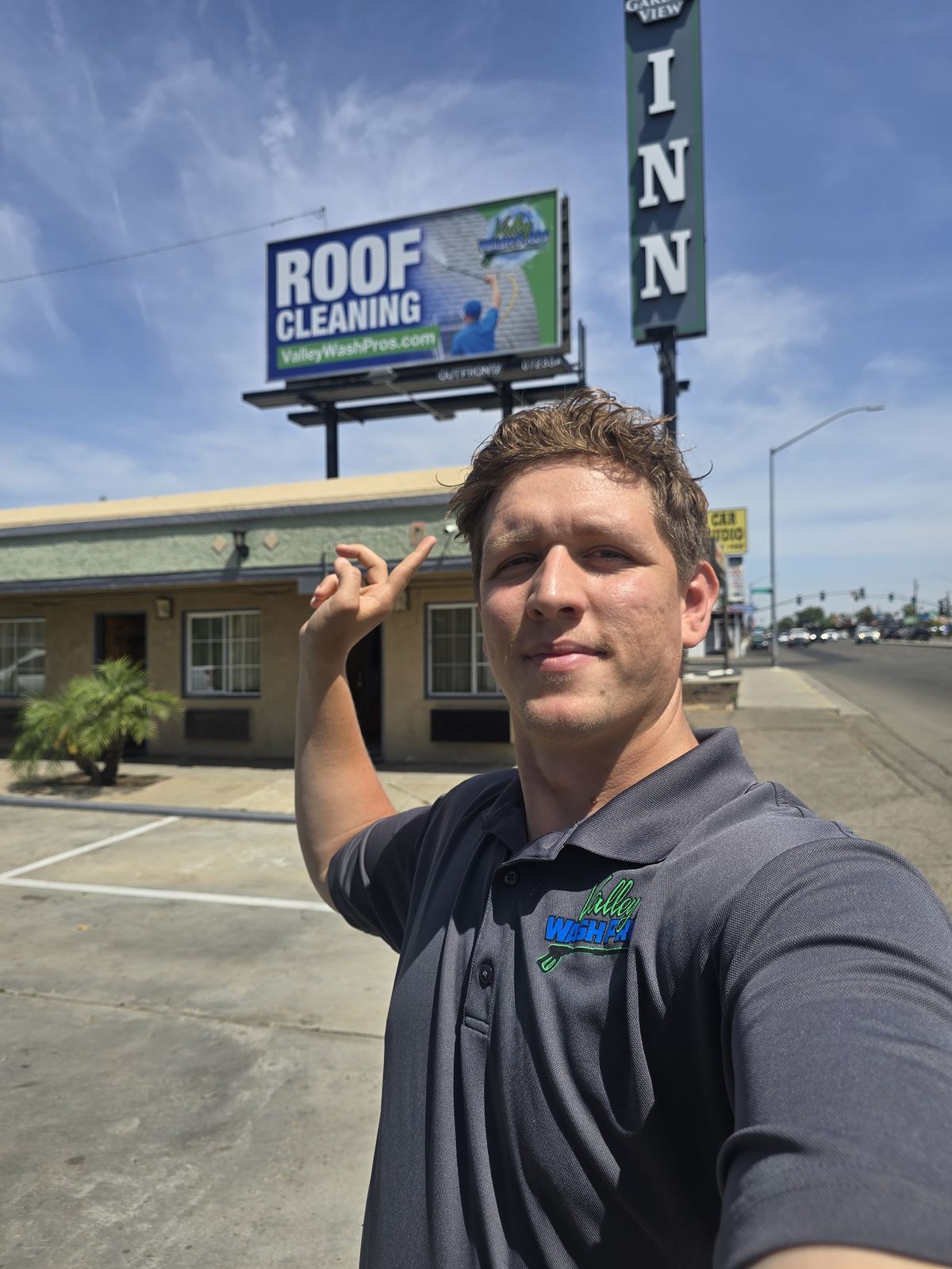 Valley Wash Pros owner pointing at the company's roof cleaning billboard in Fresno