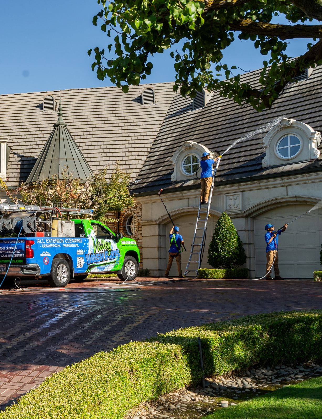 Technician on a ladder soft washing the dormers and roof of a large estate home