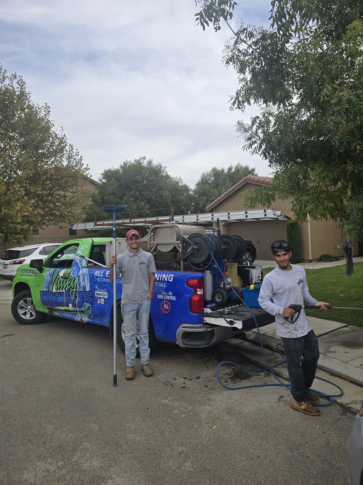 Window cleaning crew holding water fed poles beside their service truck