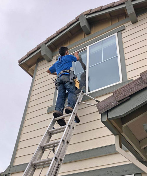 window cleaning professional on ladder cleaning window on brown home